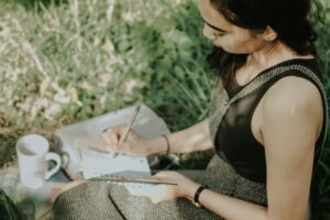 Person journaling outdoors in nature, writing in a notebook with a pen.